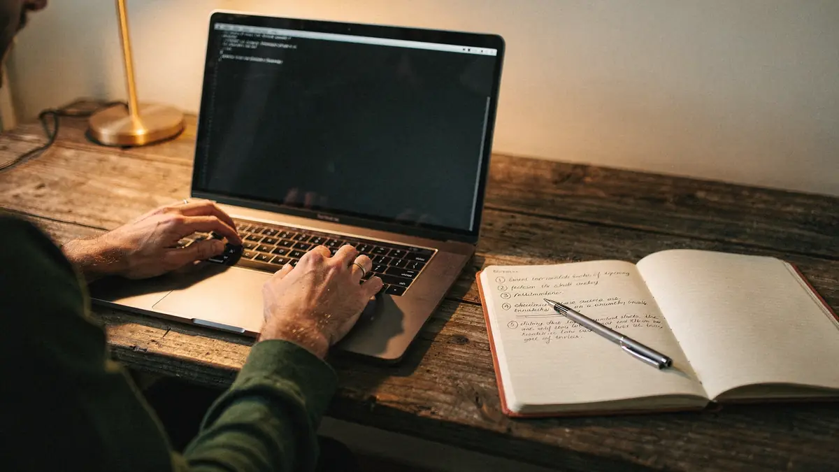 Hands at a laptop terminal with handwritten steps in a notebook alongside